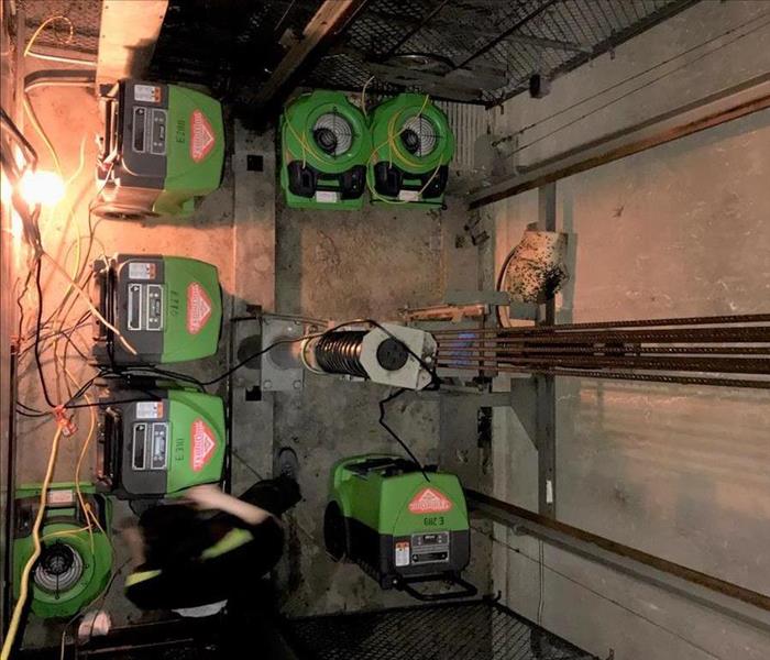 Bright green drying machines operating at the very bottom of this wet elevator shaft that had flooded on an upper level