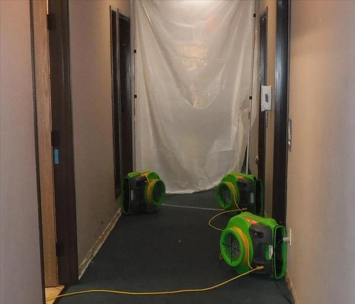 Looking down the hallway of a building, baseboards were removed and commercial fans dry-out the water damage