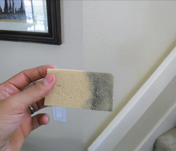A hand is holding a specialty sponge used in cleaning smoke and soot from walls. Part of the sponge is soiled grey.