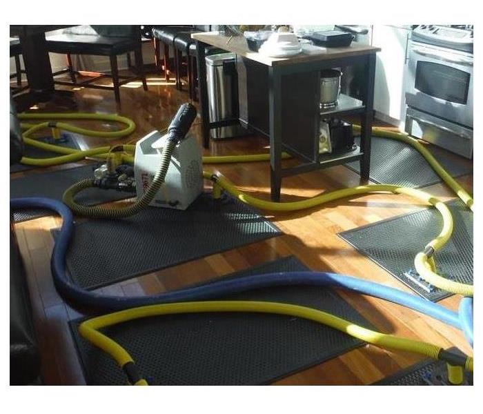 A residential kitchen is having their wood floors dried by several large vacuum matts placed as needed