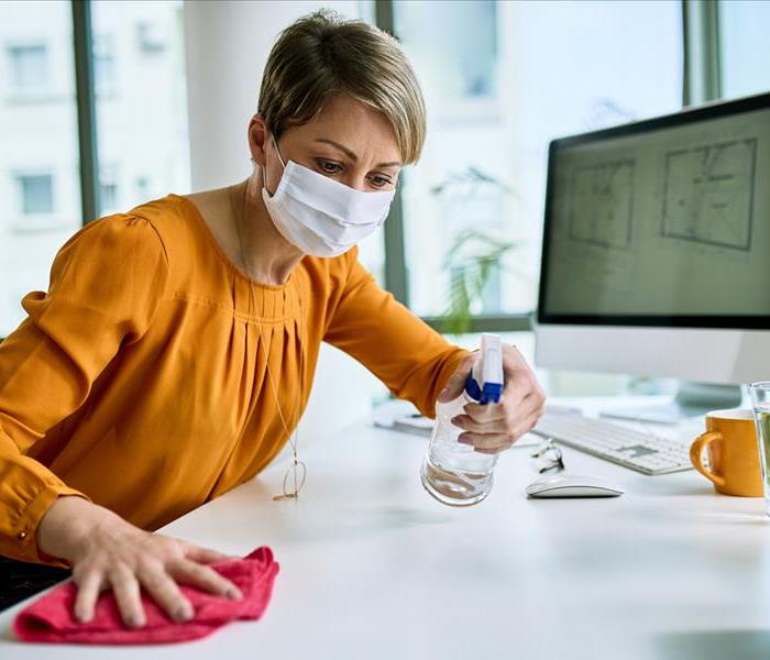 A professional woman is disinfecting her workspace and desk area to keep it fresh and clean.