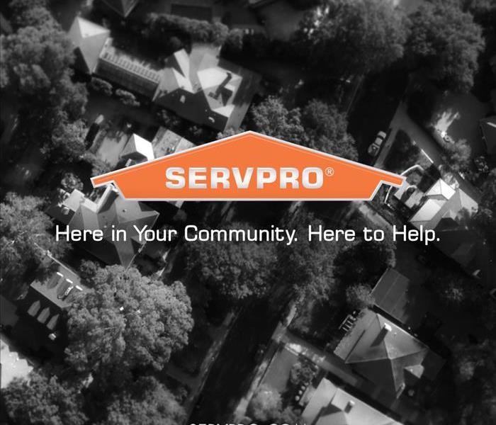 A black and white aerial view of a neighborhood of homes and a large orange house logo for SERVPRO & words: here to help